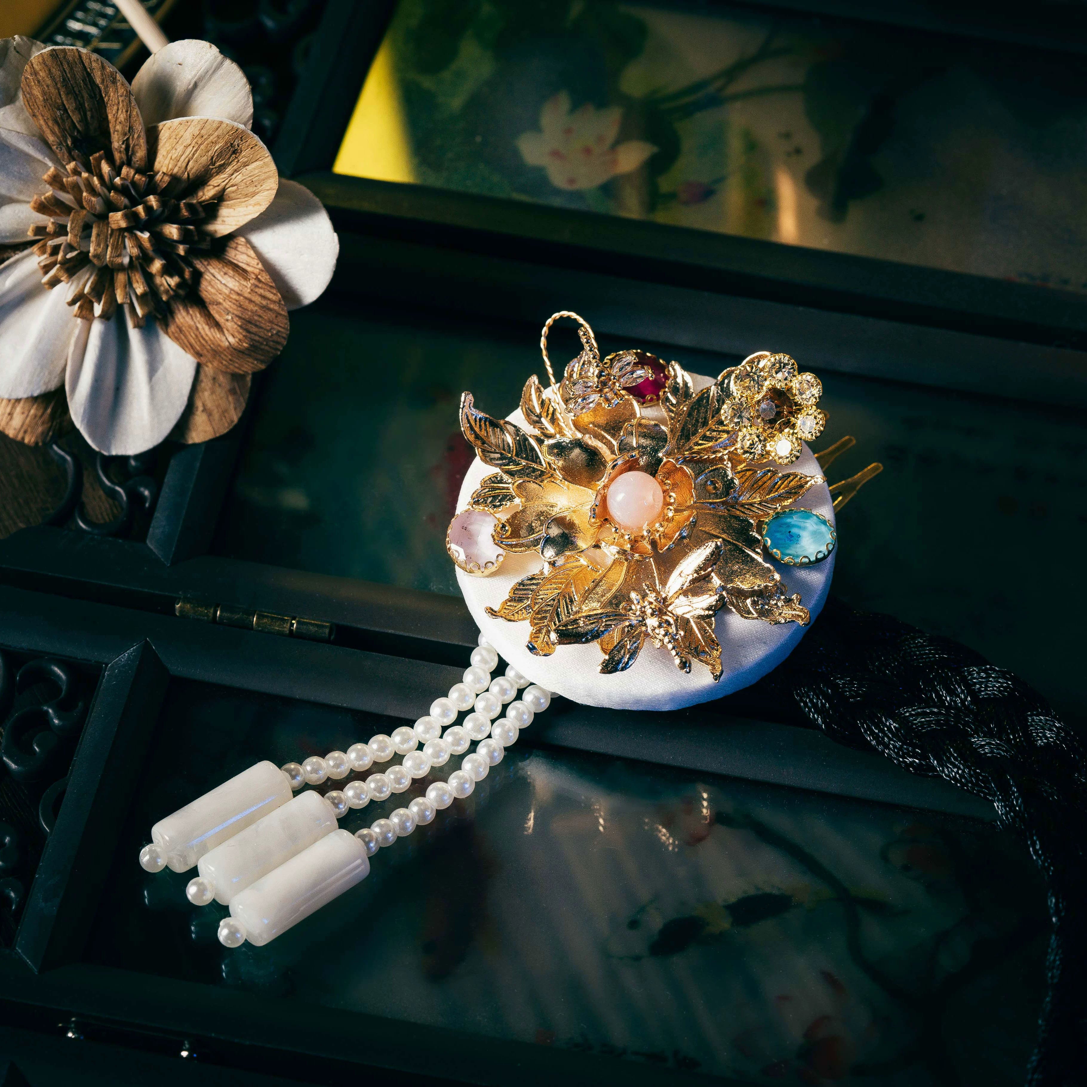 White Korean traditional ethnic headgear with gold floral design, gemstone accents, and pearl tassels, showcasing fine cutting.