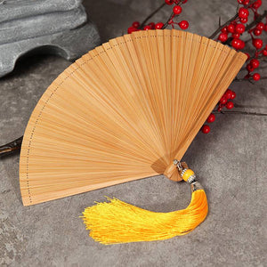 Natural bamboo fan with yellow tassel, laid flat near red berries. Full bamboo build for Hanfu dance and traditional use.