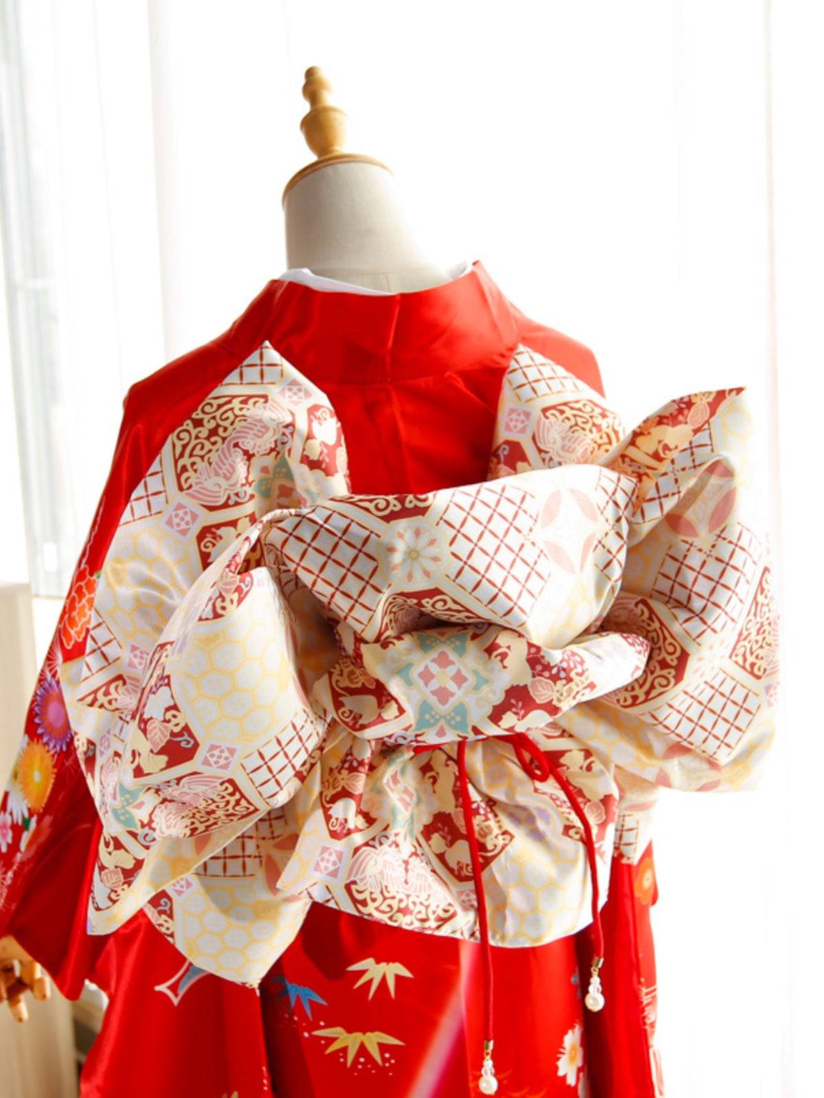 Red kimono with cream and red big three-leaf shaped bow belt featuring floral and geometric patterns. Elegant geisha-style swinging sleeve design.