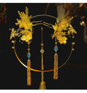 Chinese dragonfly hairpin set with gold floral design and blue accents displayed on a round stand for bridal use.