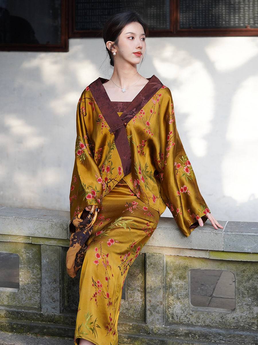 Chinese women's Golden Jelly Jacquard Dress Set with wide-sleeve jacket and floral embroidery, seated on stone bench in traditional courtyard.