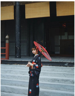 Woman in a black yukata with red floral obi belt, holding a sword and black pouch. A blend of tradition and modern elegance.