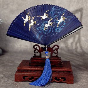 Blue Hanfu dance fan with crane and wave artwork, displayed on wooden stand. Full bamboo build with blue tassel for elegant performance use.