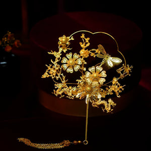 Golden floral bridal fan with butterfly and dragon details, matching Chinese wedding headdress accessories.
