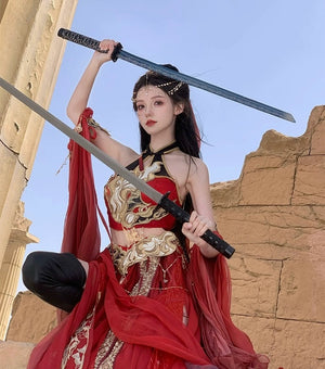 Red Sacred Flame Western Regions Dancer Hanfu with gold accents, modeled in warrior stance holding two swords near ancient ruins.