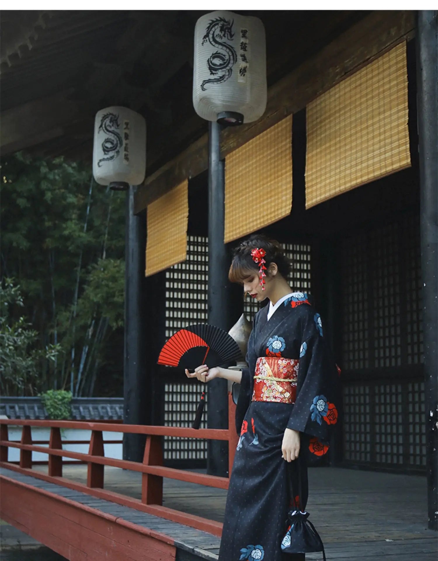 Woman in a black yukata with red floral obi belt, holding a red fan in a traditional Japanese setting. Perfect for Halloween or formal events.