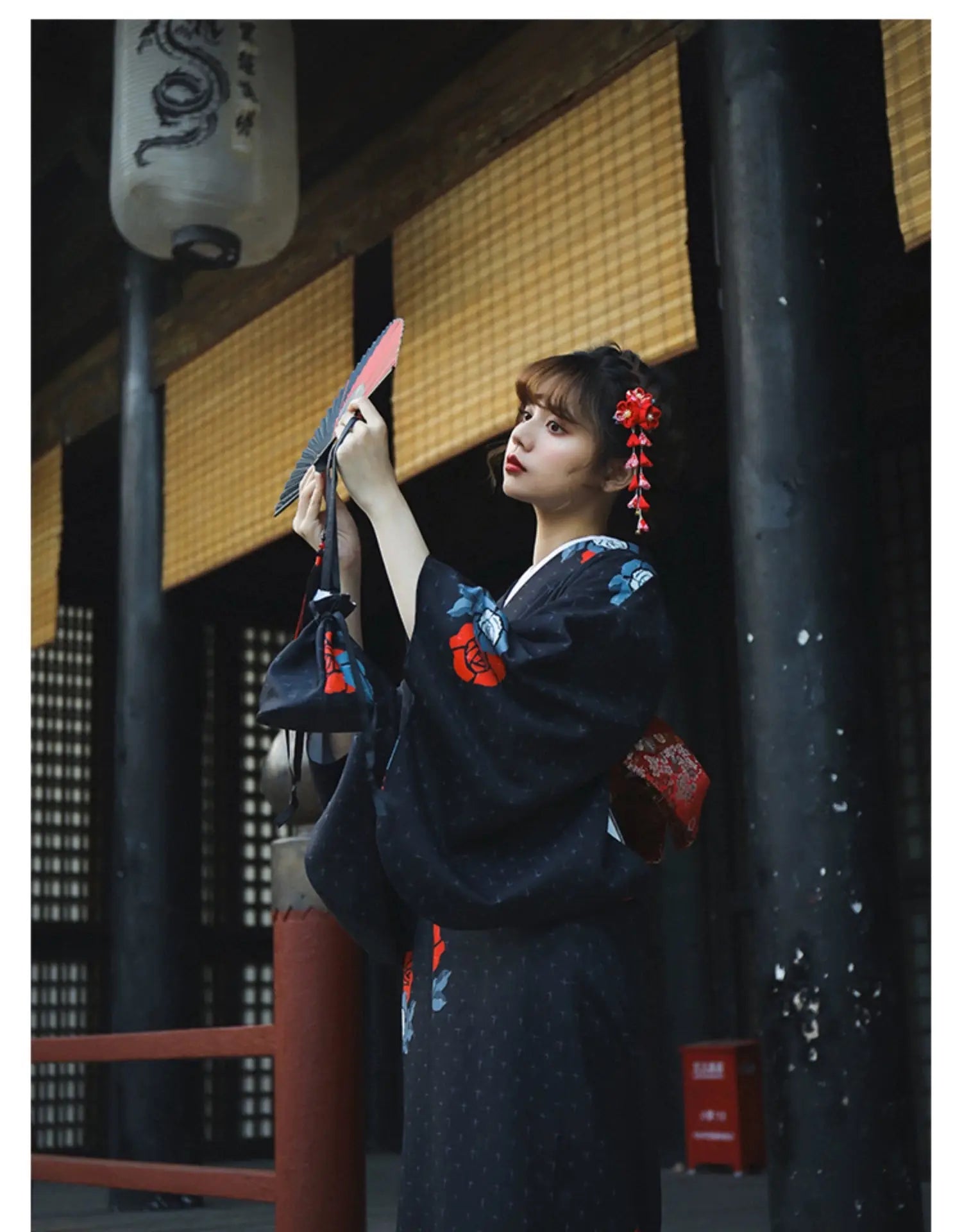 Woman in a black Japanese yukata with red floral patterns, holding a red fan in a traditional setting. A sophisticated Halloween outfit.