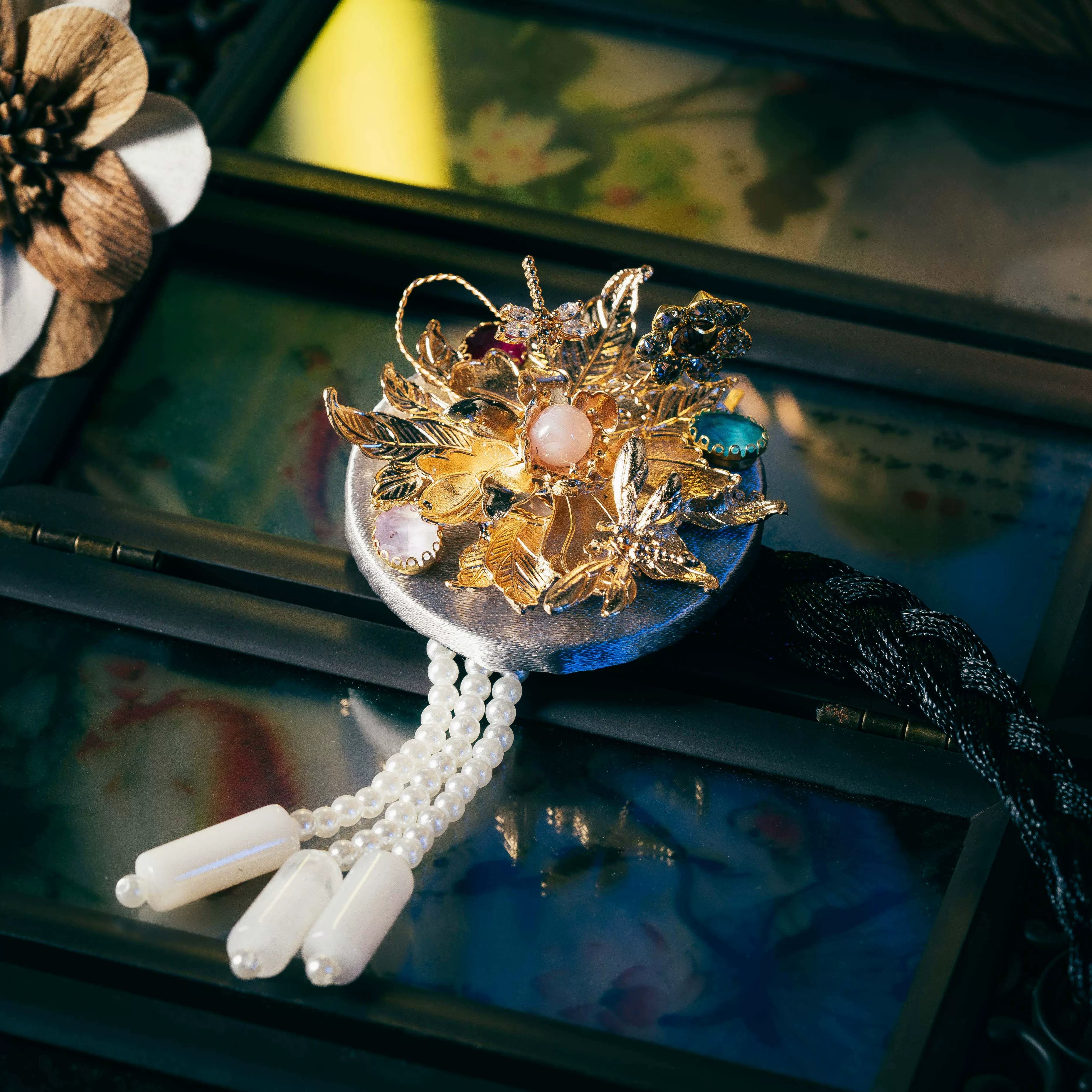 Silver Korean traditional headgear with gold floral and gemstone detailing, pearl tassels, and precise cutting craftsmanship.