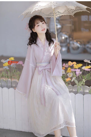 Modern Hanfu dress in pastel pink with lace skirt, styled with parasol and floral accessories for a romantic spring look.