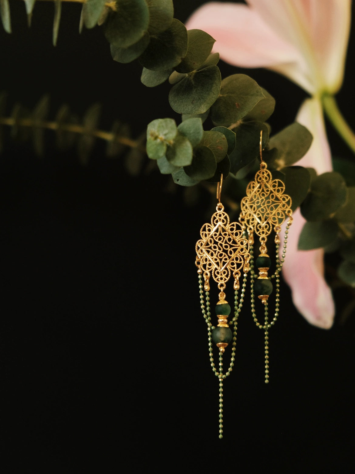 Su Mask Ear Clips - Hanfu Gold Tassel Earrings with green chalcedony beads, hanging on eucalyptus with soft pink lily in background.