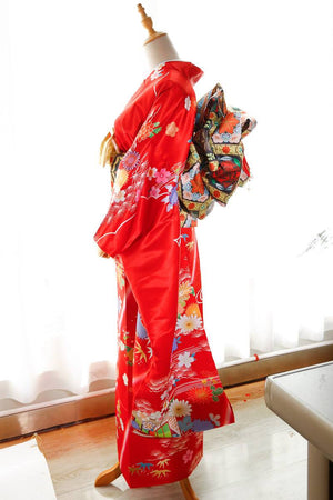 Full side view of red floral kimono with swinging sleeves and black patterned big three-leaf bow belt. Geisha-style fashion accessory.