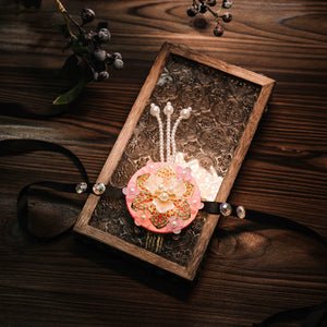 Pink Korean traditional headgear with floral pearl design and beaded hairpins, placed on ornate wooden tray.