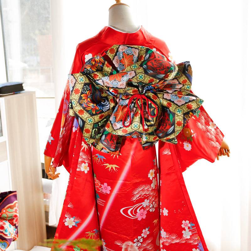 Back view of red kimono with swinging sleeves and large floral-patterned three-leaf bow belt. Traditional geisha-style belt design.
