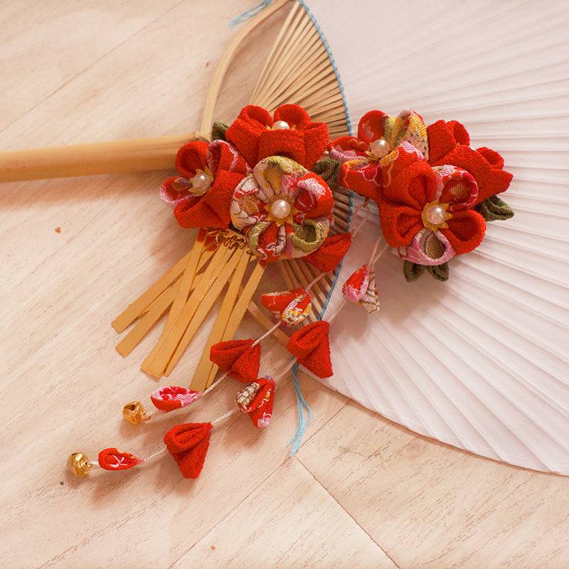 Japanese handmade crepe hair accessories hairpins featuring red floral designs with pearl centers and gold combs, styled on a wooden fan.