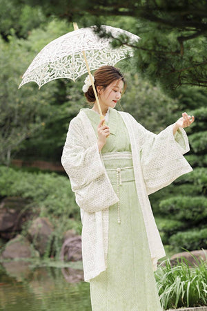 Model in green lace kimono and waist seal bow, styled with a white lace outer layer and parasol in a garden setting.