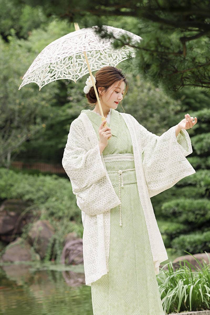 Model in green lace kimono and waist seal bow, styled with a white lace outer layer and parasol in a garden setting.