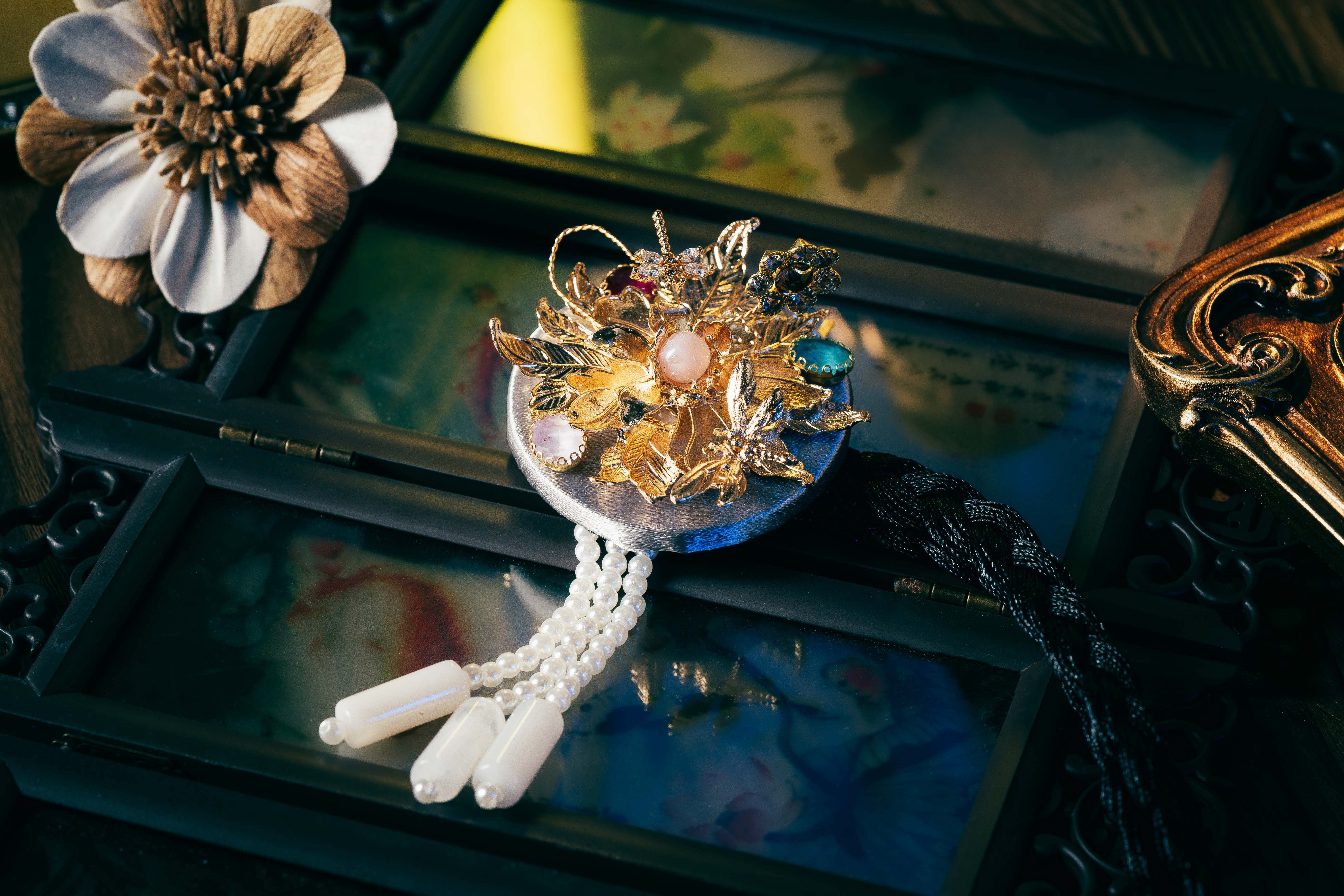 Silver Korean traditional headgear with gold floral motifs, colorful stones, and pearl tassels, crafted with precision cutting.