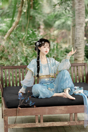 Model in blue Hanfu Princess Jasmine ethnic suit by 【Cloud Traveler】, seated on a wooden bench with floral accessories.