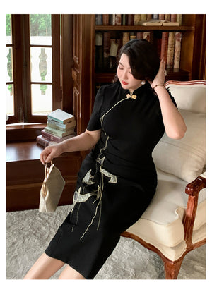 Plus size black cheongsam/qipao dress with gold bird embroidery, styled in a vintage armchair setting with bookshelves.