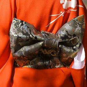 Black floral brocade bow belt styled with red kimono, ideal for traditional Japanese yukata waist styling and festive occasions.