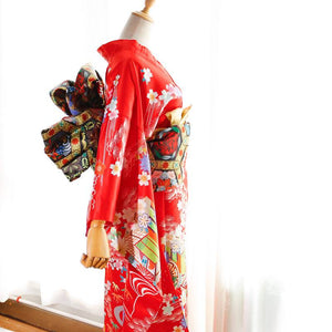 Side view of red kimono with gold-accented floral bow belt. Swinging sleeves and big three-leaf bow enhance geisha-inspired style.
