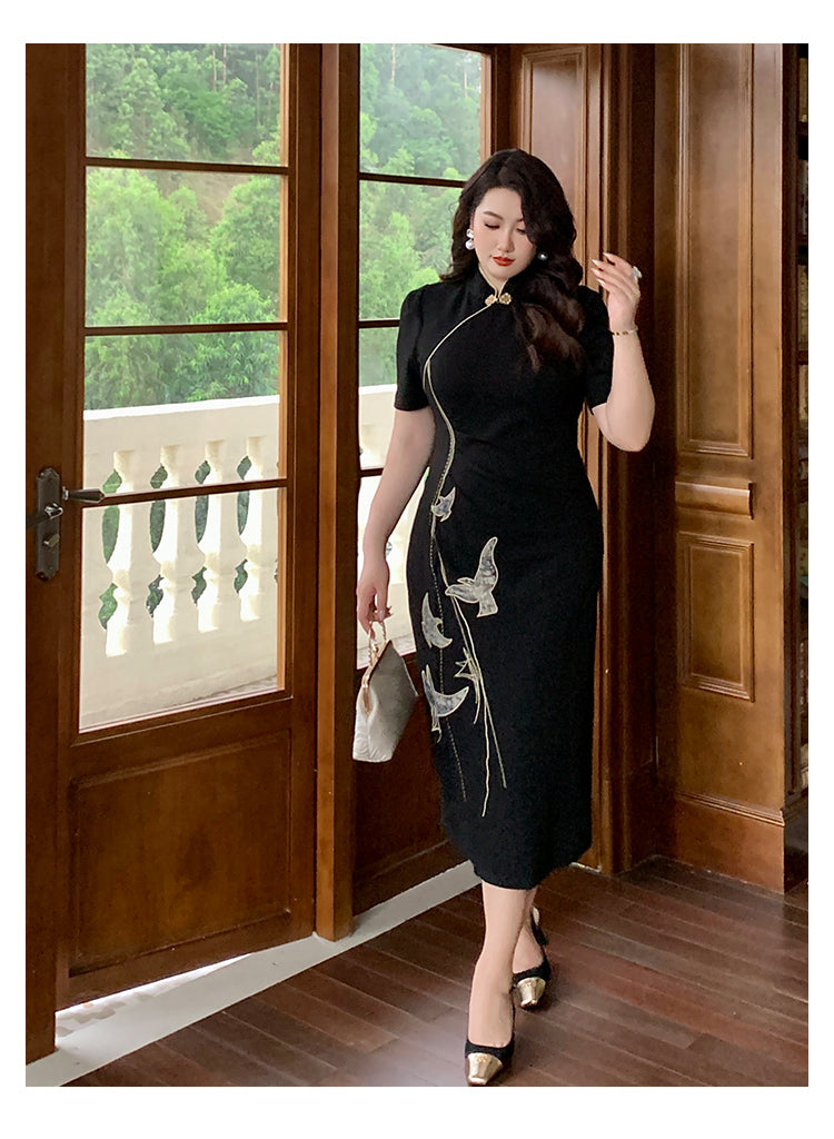Black embroidered plus size qipao dress with gold bird design, styled with heels and handbag in a wooden interior.