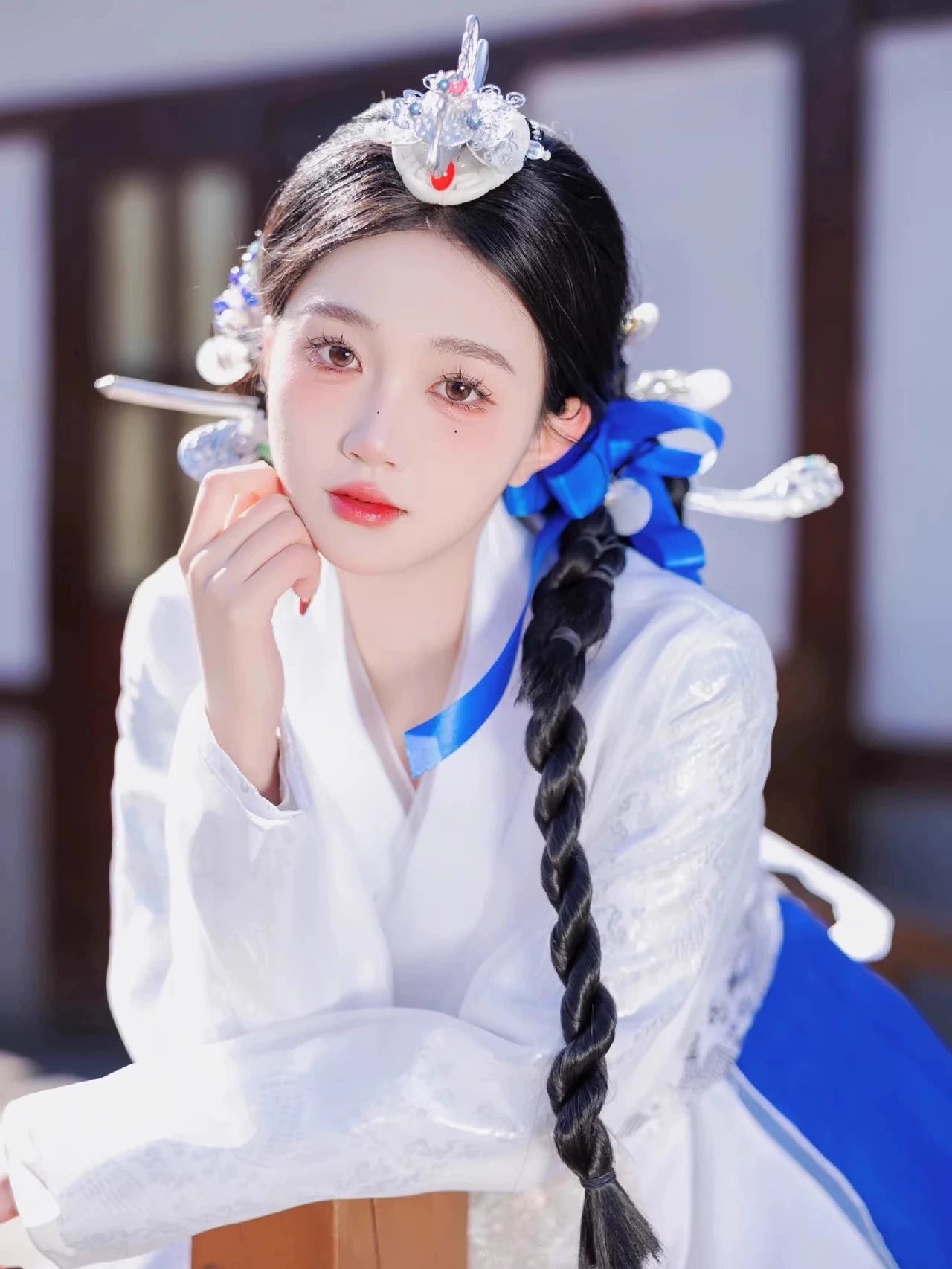 White embroidered hanbok top with silver headpiece, braided hair with blue ribbon - close-up portrait