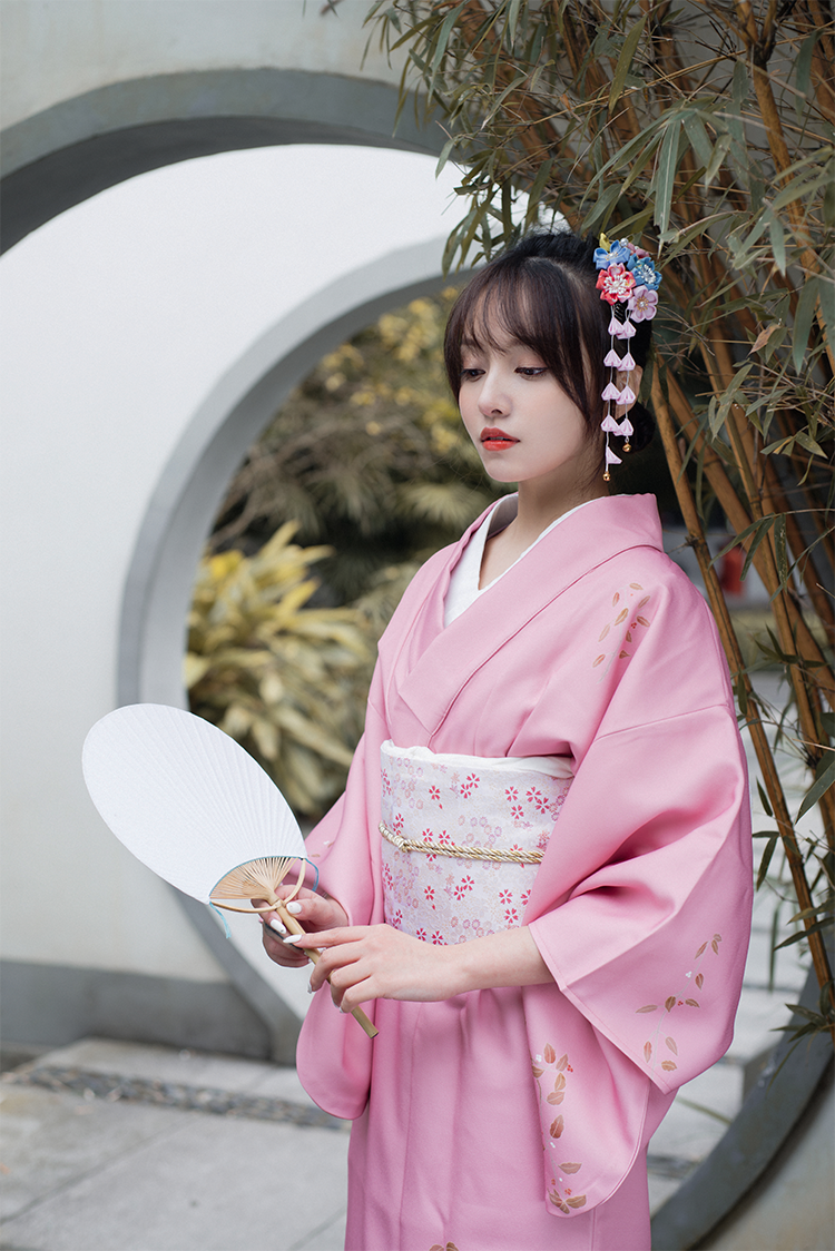 Woman in pink kimono holding fan, adorned with Japanese crepe floral hair comb with pink tassels, ideal for Hanfu photo sessions.