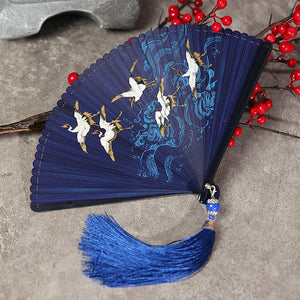 Blue bamboo Hanfu fan with crane design and blue tassel, laid flat. Elegant accessory for traditional Chinese performances.