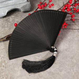 Elegant black bamboo fan with black tassel, folded and placed near red berries. Ideal for Hanfu dance and traditional performances.