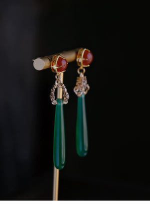 Elegant green agate drop earrings with red gemstone tops and gold detailing, displayed on a black background for a luxury look.