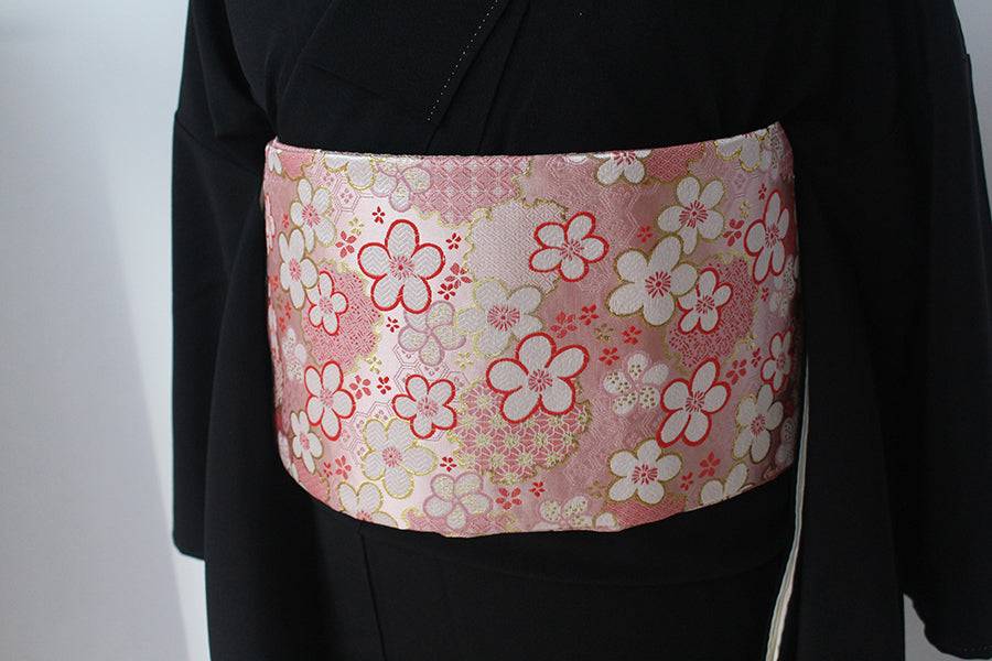 Flat view of pink floral kimono brocade waist seal without bow, worn over black kimono. 120cm reversible accessory with gold accents.