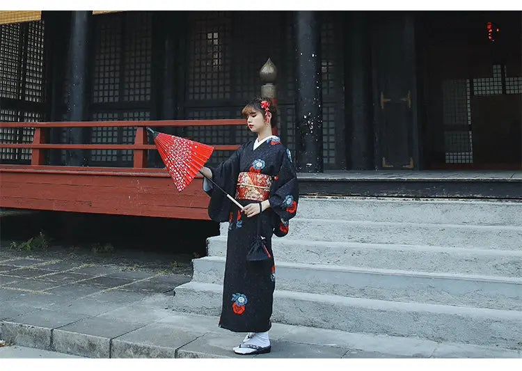 Full-length view of a woman in a black yukata with red floral obi belt, holding a red umbrella. Perfect for formal or Halloween-themed events.