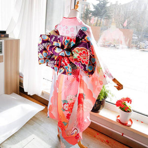 Back view of pink kimono with vibrant purple big three-leaf bow belt. Swinging sleeves and geisha-style belt bag complete the look.