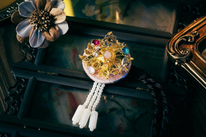 Pink Korean traditional headgear with gold floral design, gemstone accents, and pearl tassels, showcasing fine cutting craftsmanship.