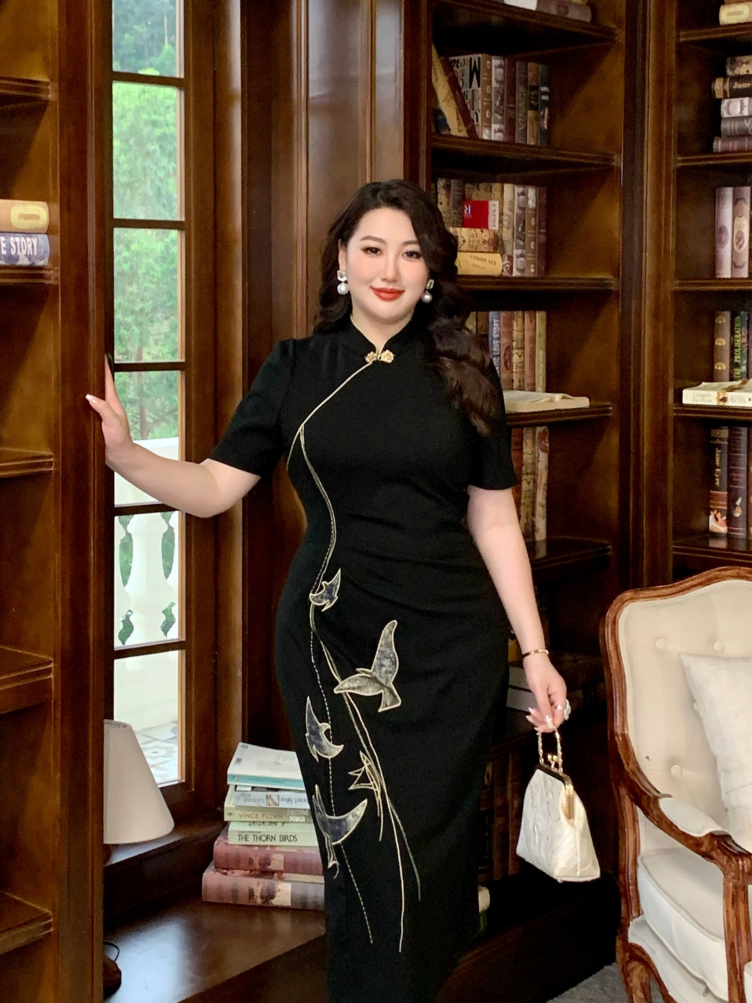 Elegant black plus size qipao dress with traditional Chinese embroidery, modeled in a classic wood-paneled library.