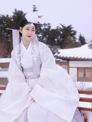 White Yanji Hanbok court dress with floral embroidery, worn in snowy setting, traditional Korean attire for winter elegance.