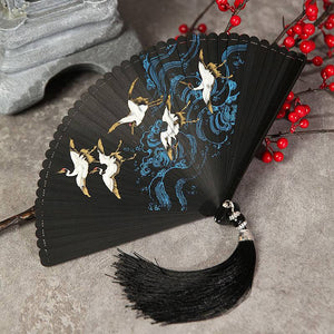 Black bamboo Hanfu fan with crane and wave artwork, laid flat with black tassel. Perfect for traditional Chinese dance.