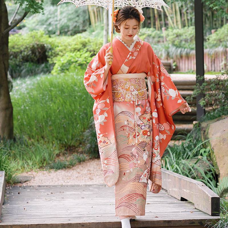 Model wearing full kimono with pink brocade waist seal and bow, styled with parasol in garden. 120cm reversible accessory.