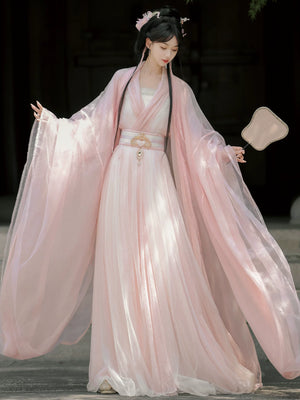 Woman in a traditional pink dress with flowing sleeves against a dark background