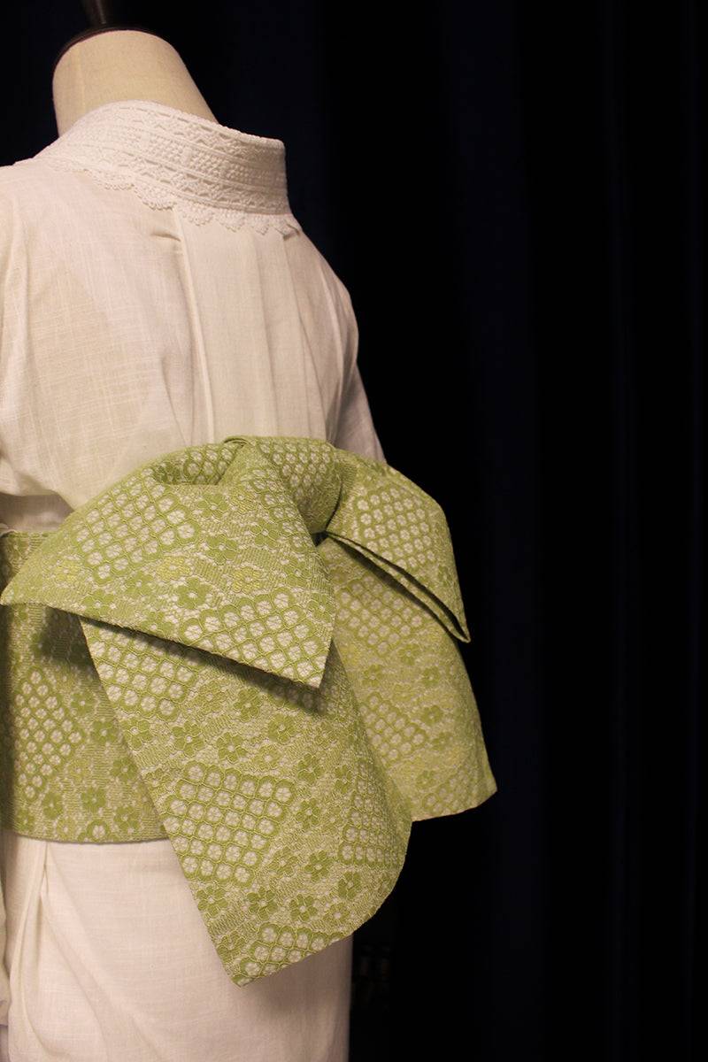 Angled view of green lace composite kimono waist seal bow on white kimono, emphasizing its layered and voluminous design.