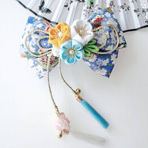Blue floral Japanese kimono hair clip with yellow, white, and turquoise cherry blossoms, gold bow, and teal tassels.