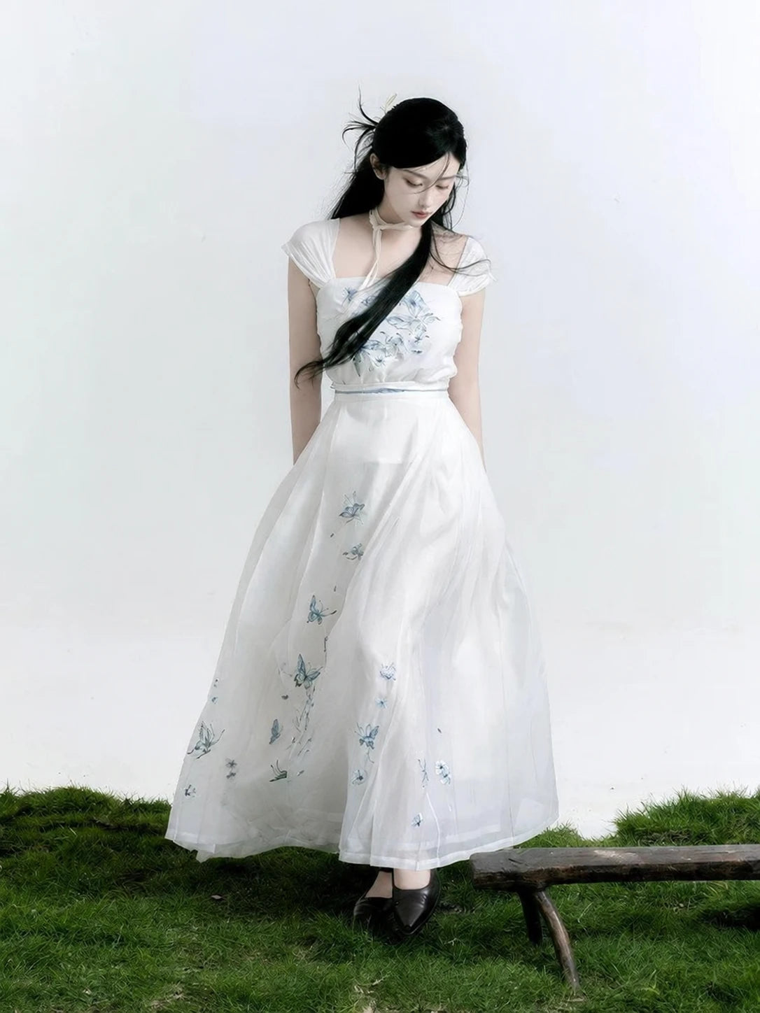 Model looking down at a white butterfly Hanfu camisole and flowing white mamian skirt with blue embroidery