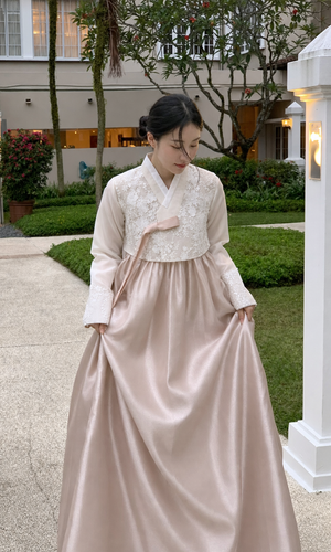 Woman wearing ivory floral lace and champagne blush modern hanbok rental set in a garden