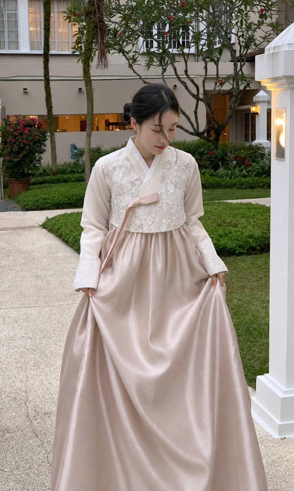 Woman wearing ivory floral lace and champagne blush modern hanbok rental set in a garden