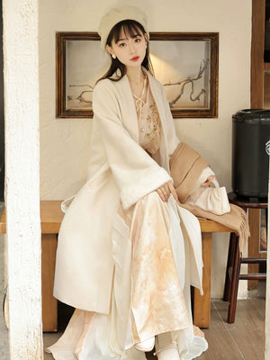 Seated view of the apricot Hanfu coat outfit showing the wide sleeve and layered skirt hem