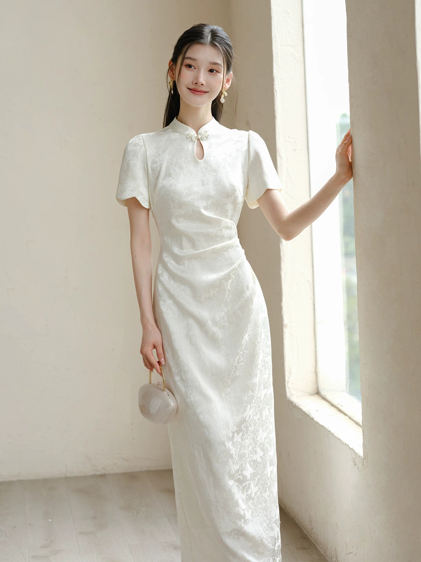 Front styling view of the Soft White jacquard pleated qipao dress, with subtle jacquard, fitted waist, front pleats and keyhole mandarin collar.