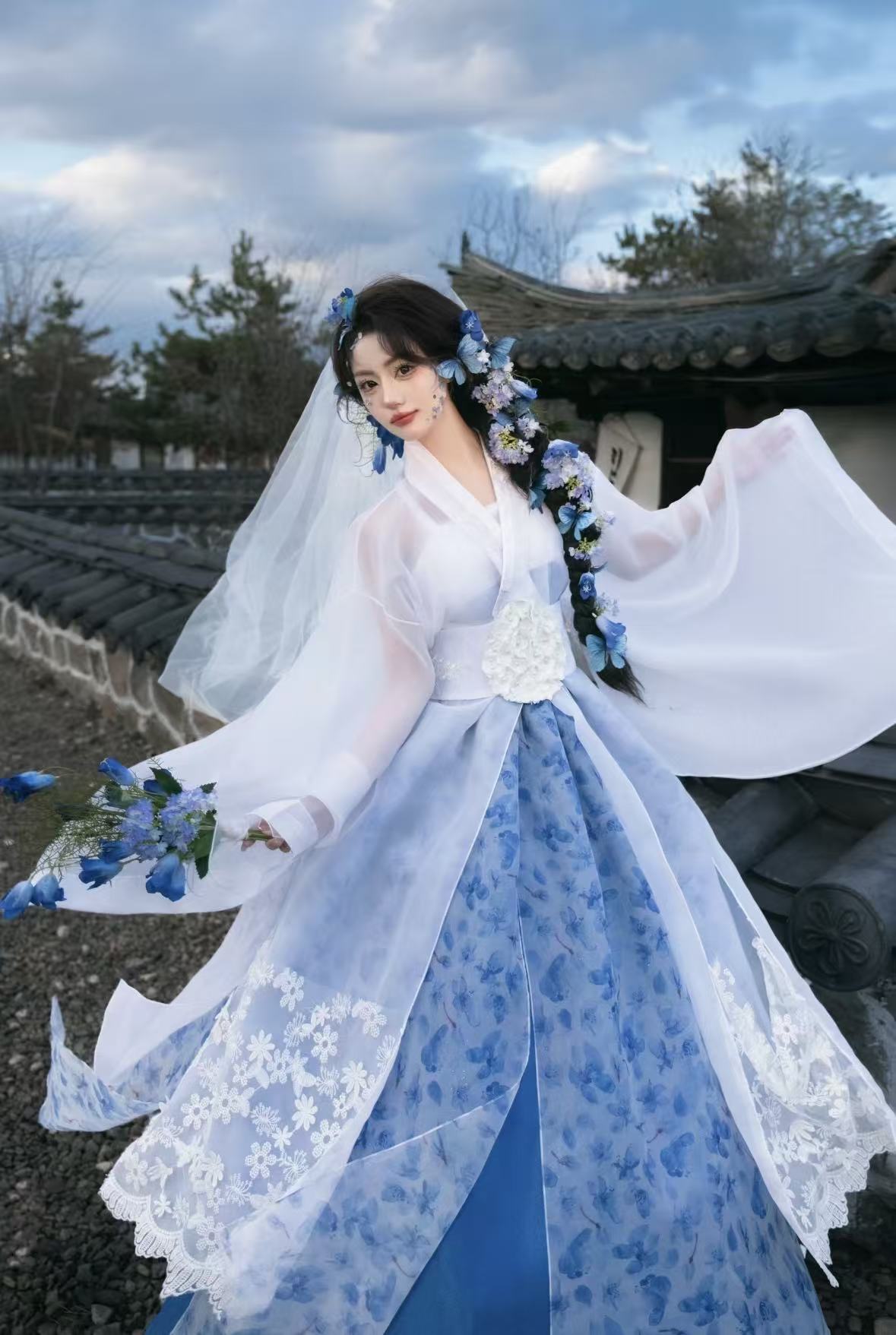 Person in traditional blue and white dress with floral accessories outdoors.