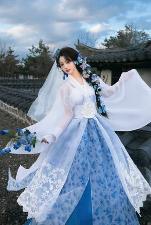 Person in traditional blue and white dress with floral accessories outdoors.