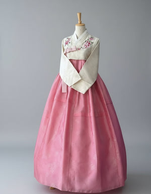 Traditional Korean hanbok with pink skirt and white top on a mannequin against a decorative wall.